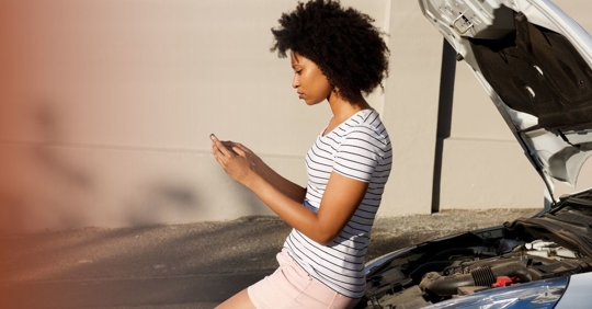 Woman on cellphone sitting on open hood of car