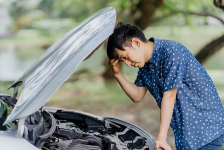 confused person looking under hood of car