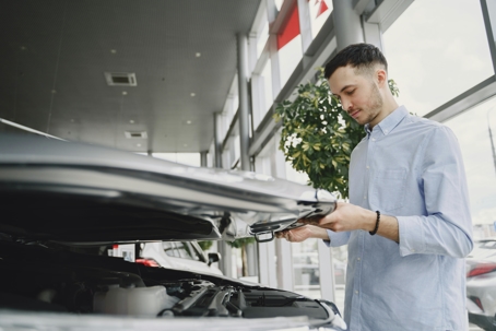 car buyer looking under hood of vehicle in showroom